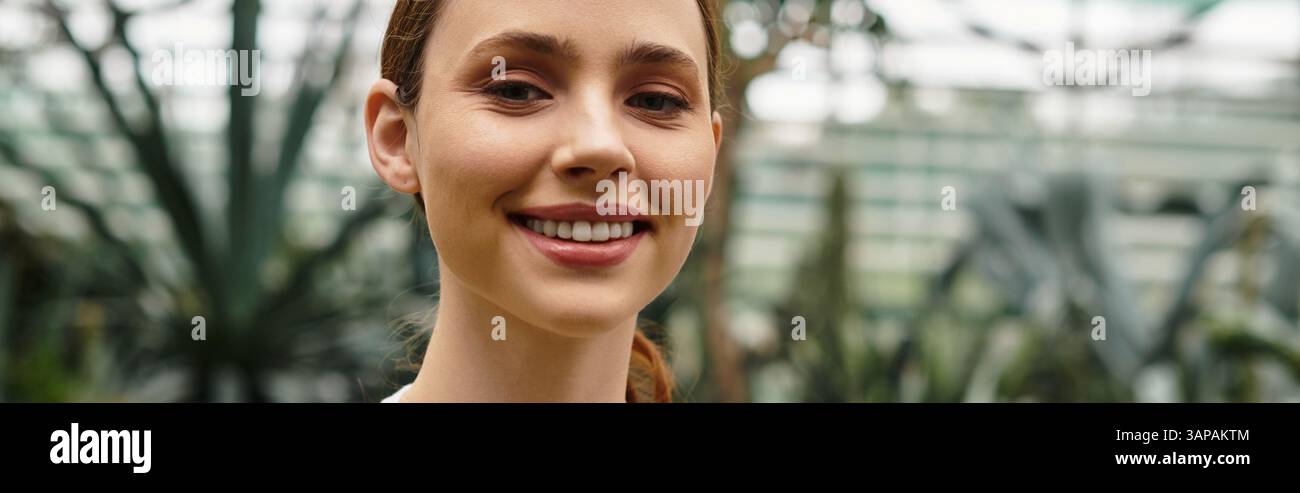 Beautiful young woman smiles warmly amidst thriving plants in a bright ...