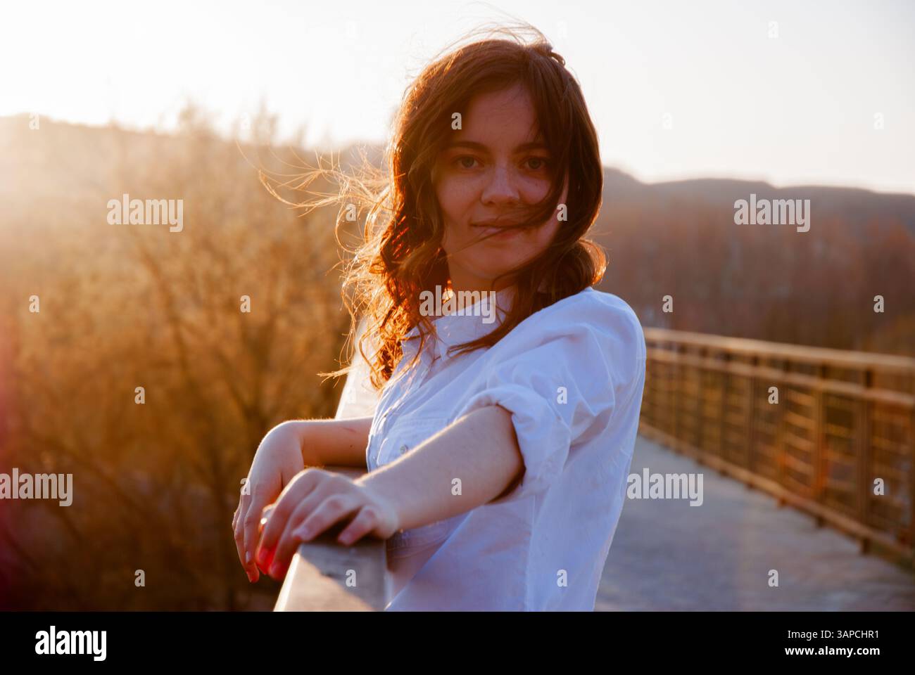 Woman enjoying a serene sunset on a bridge during autumn. Stock Photo