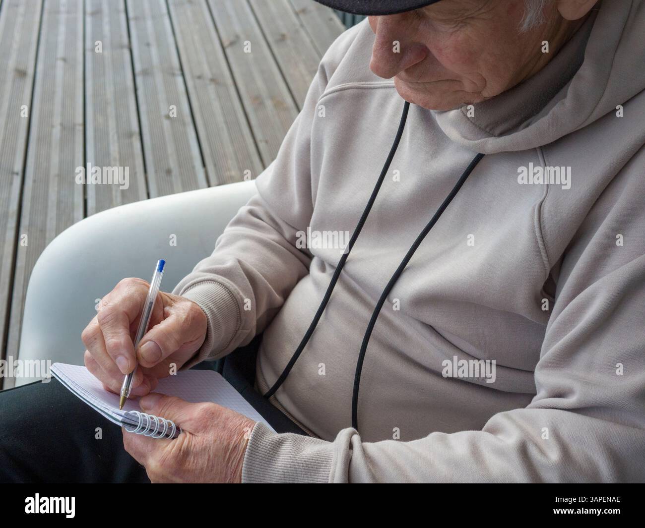 Focused elderly person writing notes in notebook, sitting on white ...