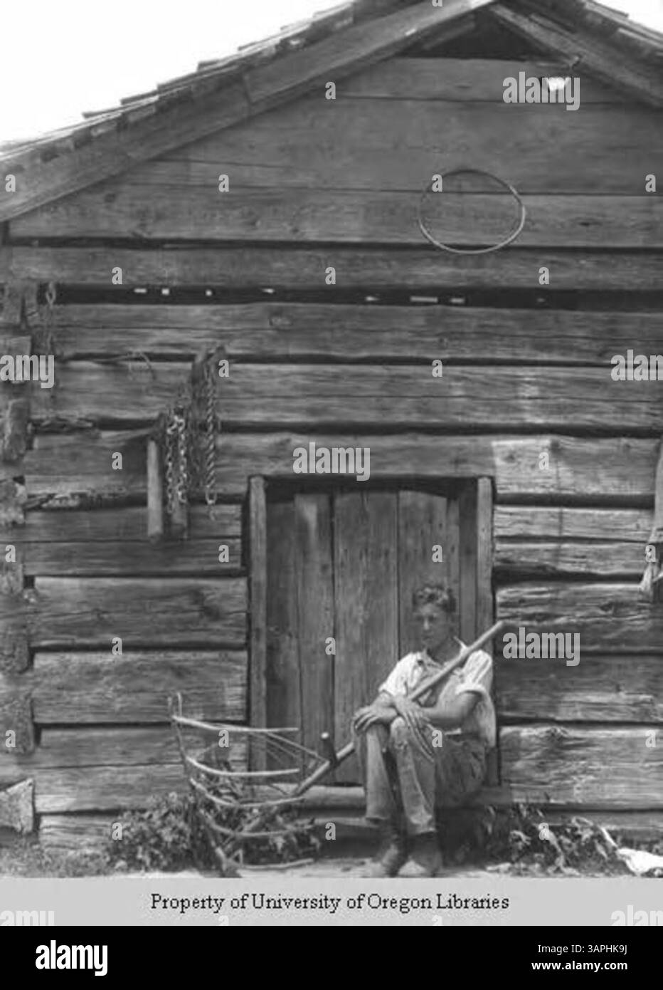A photograph showing a young man sitting outside a shed with a hay rake ...