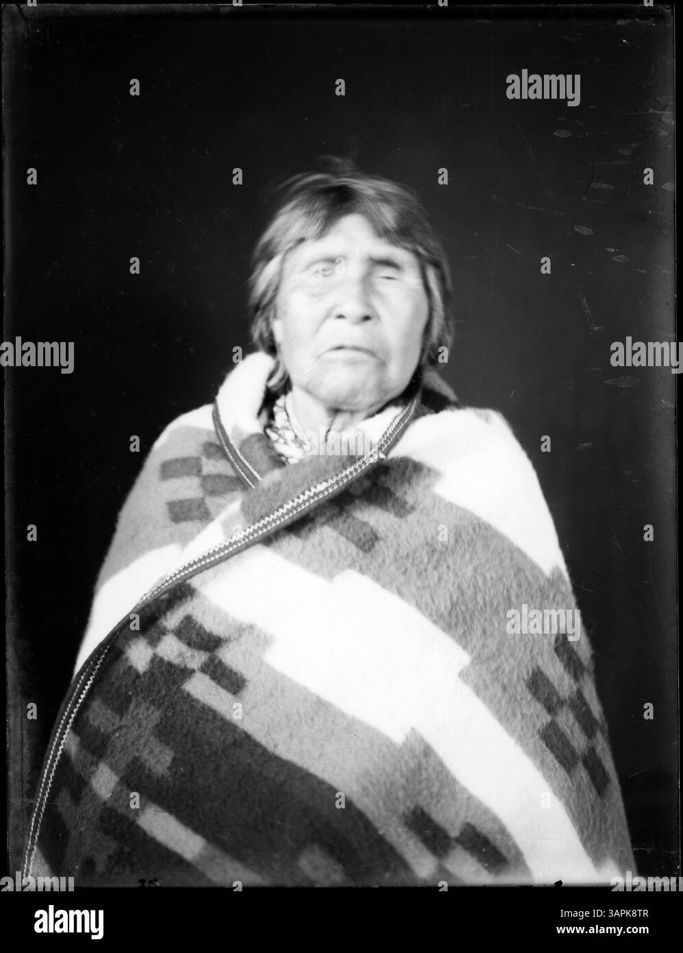 This portrait captures a Native American man wrapped in a blanket ...