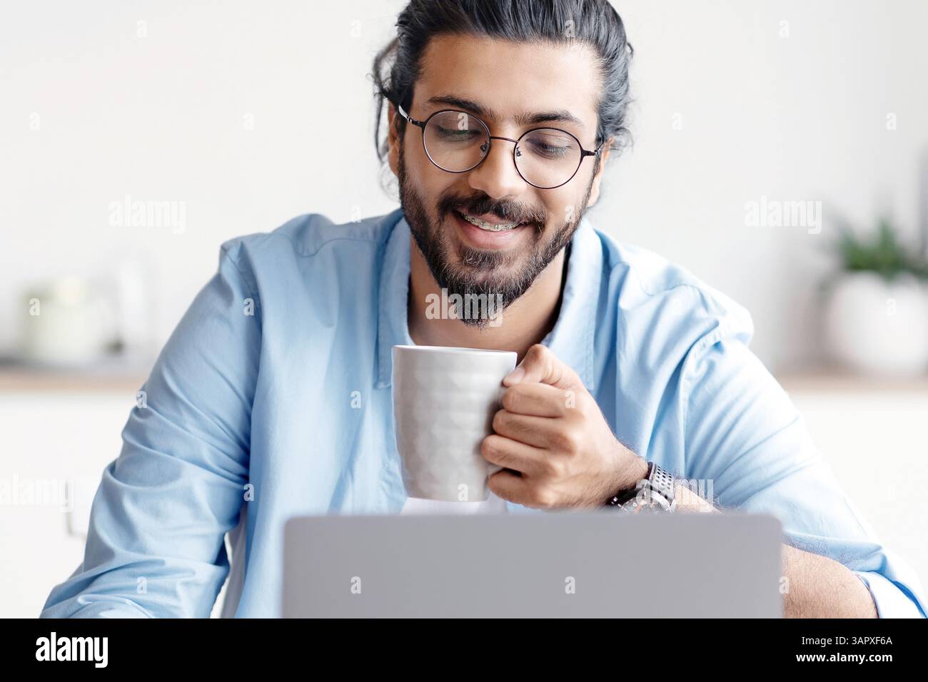 Young Smiling Arab Freelancer Guy Using Laptop And Drinking Coffee At Home Stock Photo
