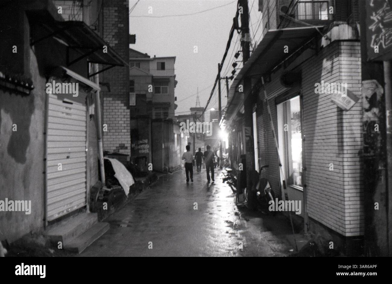 Evening stroll through a quiet alley in a bustling city, revealing the intimate pulse of urban life and its hidden: Urban Alley at Night in Southern China - Early 2000s Street Life and Residential Scene Stock Photo