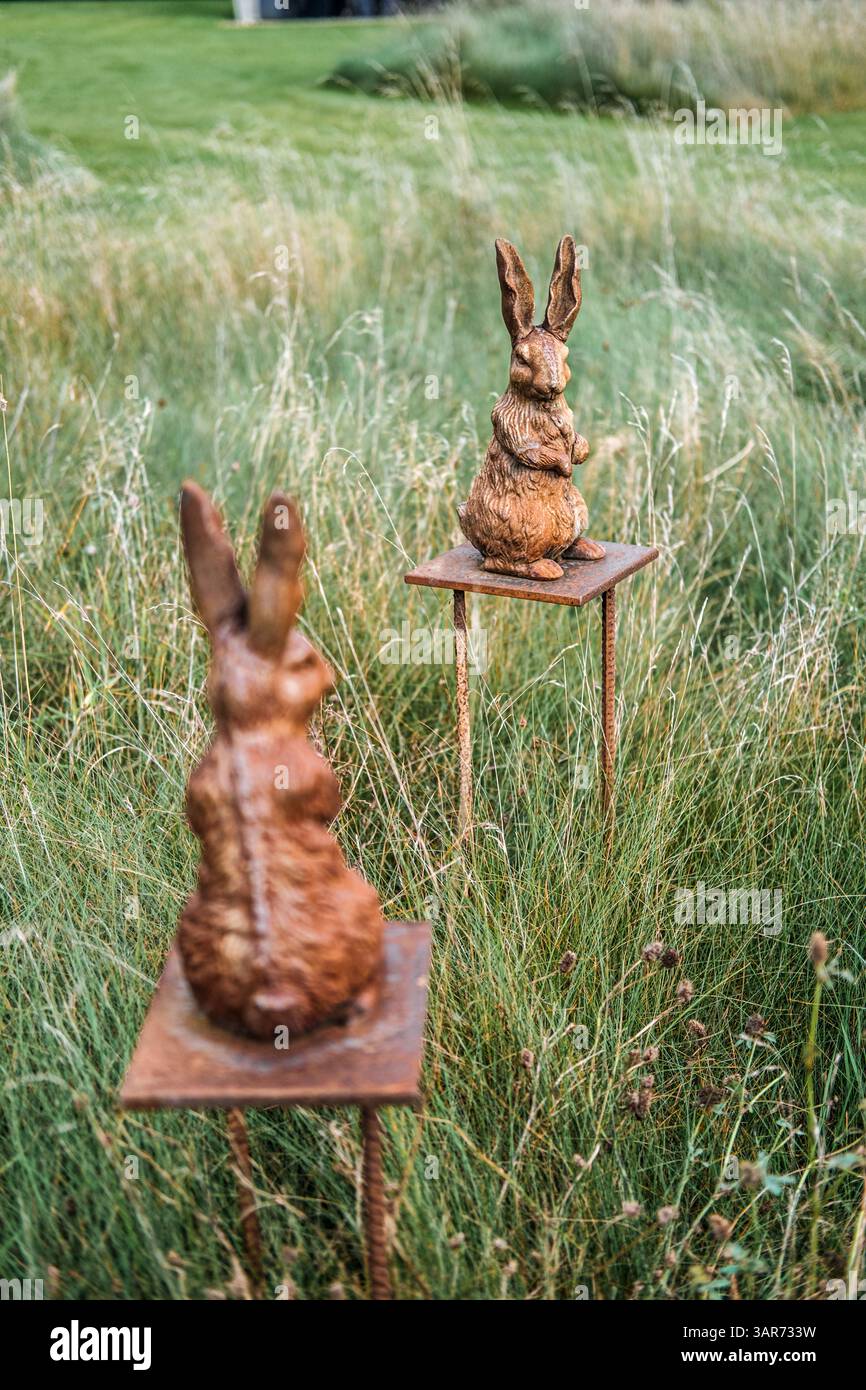 Two rust-colored rabbit sculptures on metal stands placed in tall ...