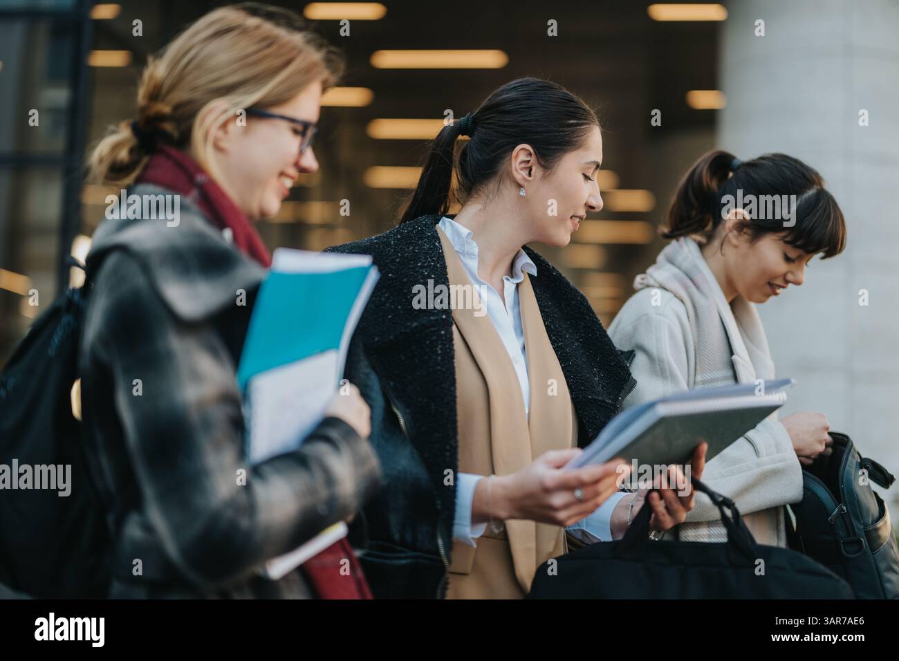 Three businesswomen collaborating outdoors while reviewing documents and sharing ideas Stock Photo
