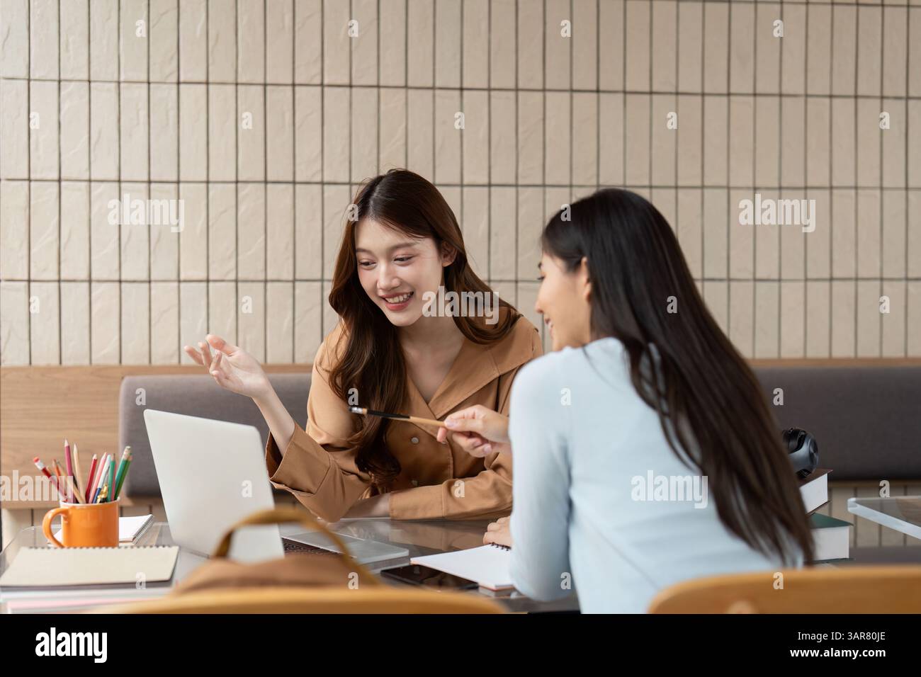 Collaboration and Creativity. Two students share ideas and knowledge while using a laptop in a shared study space. Stock Photo