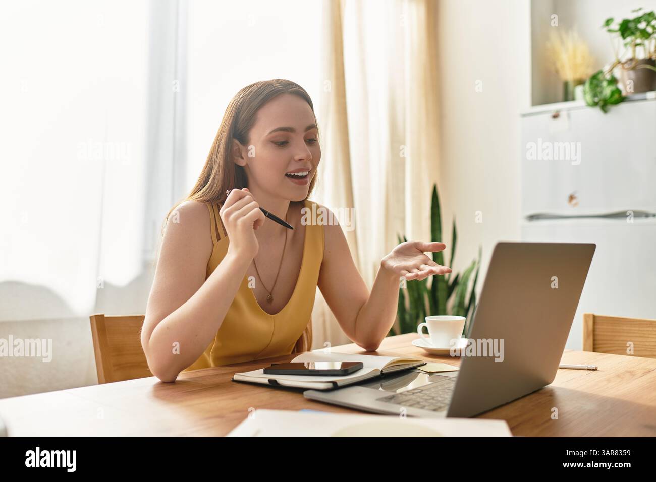 A young woman chats excitedly online at her kitchen table. Stock Photo