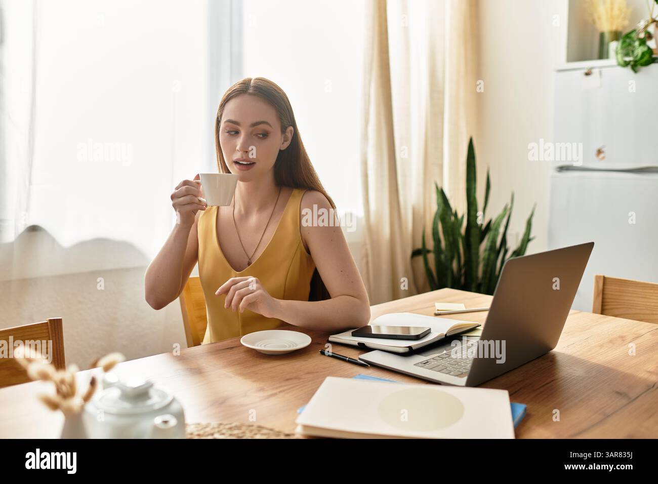 A young woman enjoys her coffee at a cozy table by sunlit windows. Stock Photo