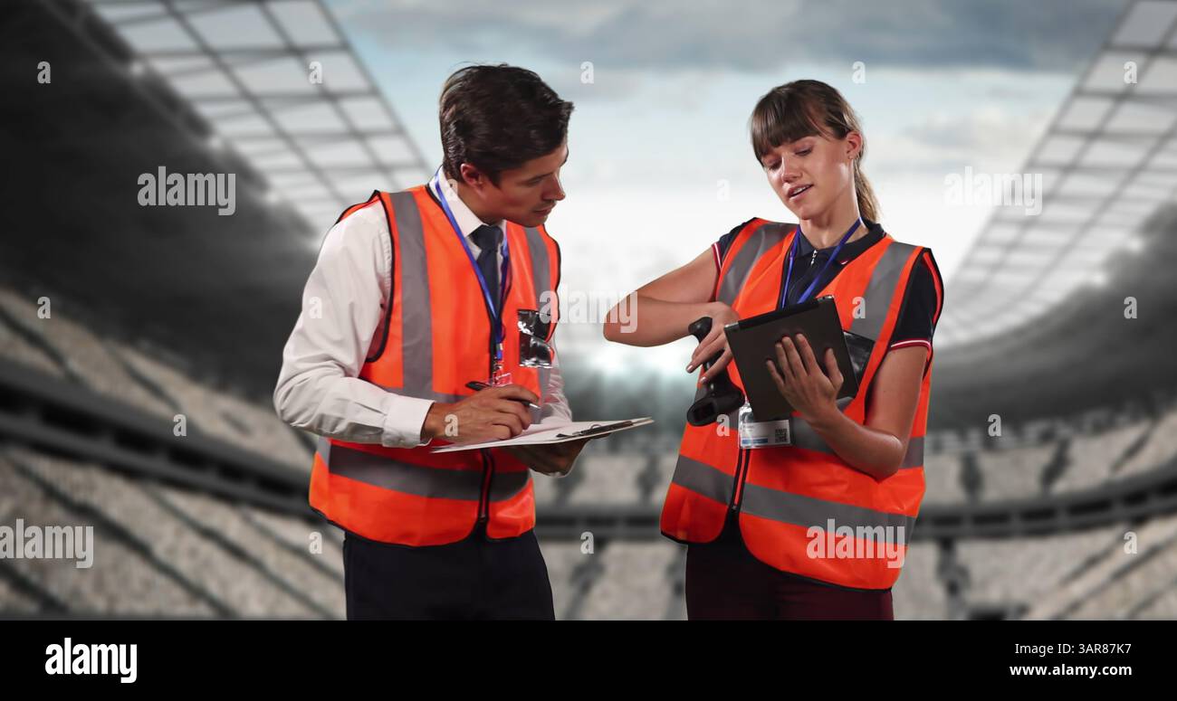 Image of stadium over caucasian male and female workers talking and using tablet Stock Photo