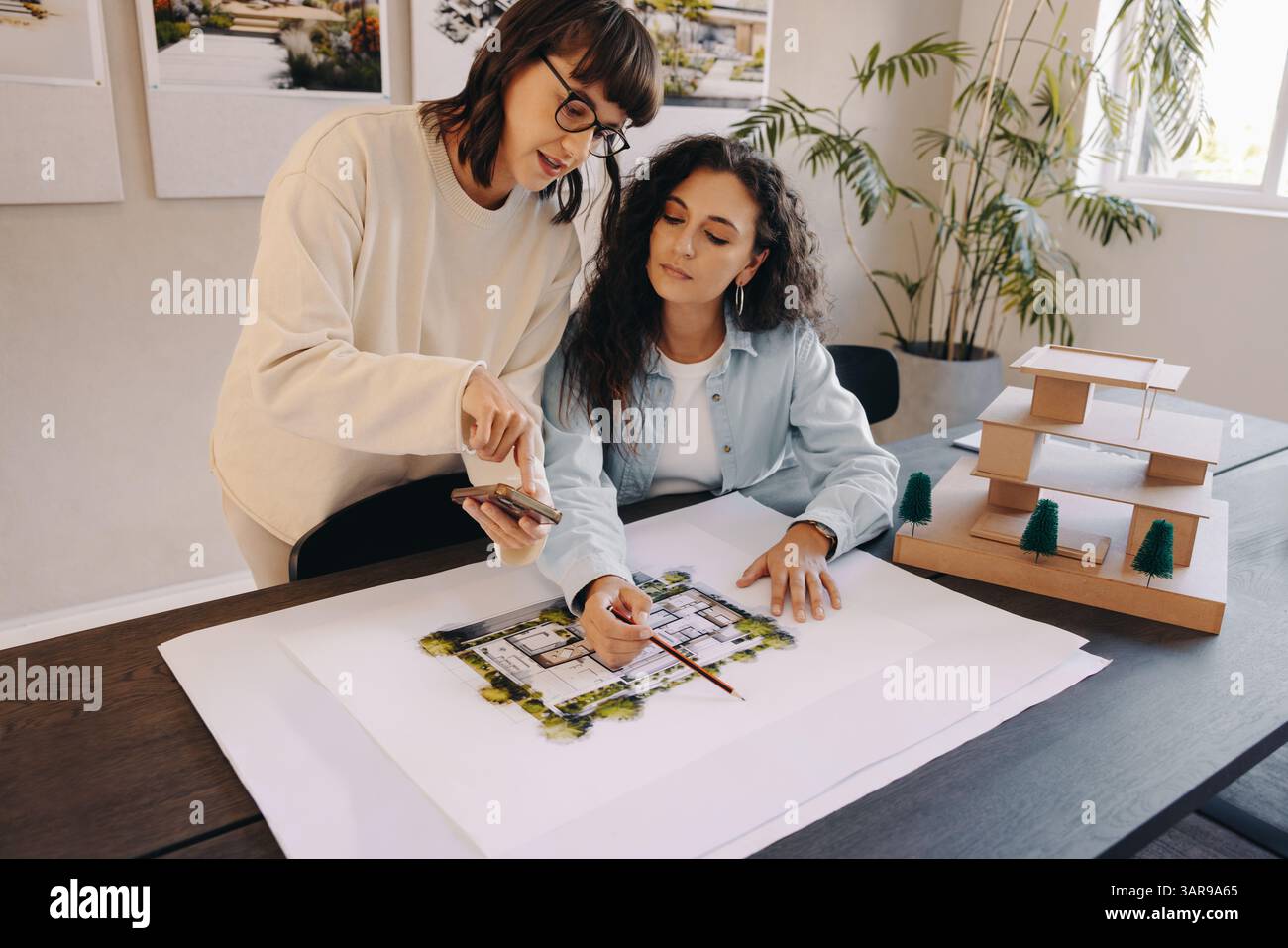 Architects reviewing draft plans while collaborating in a bright workspace featuring a wooden scale model. Stock Photo