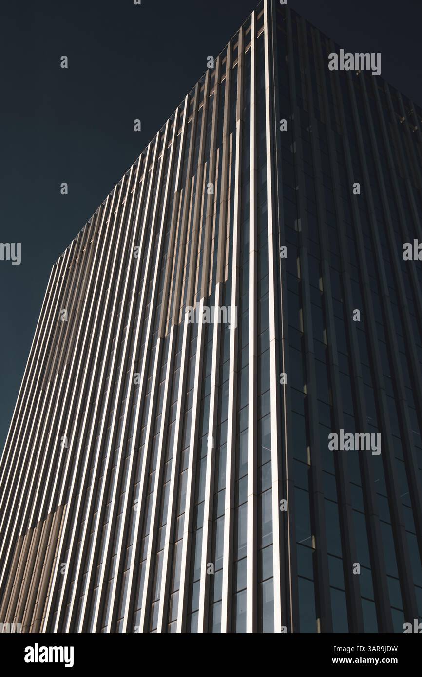An impressive modern skyscraper reaches into a clear blue sky, showcasing architectural prowess and design. The building has sleek lines. Urban scene. Stock Photo
