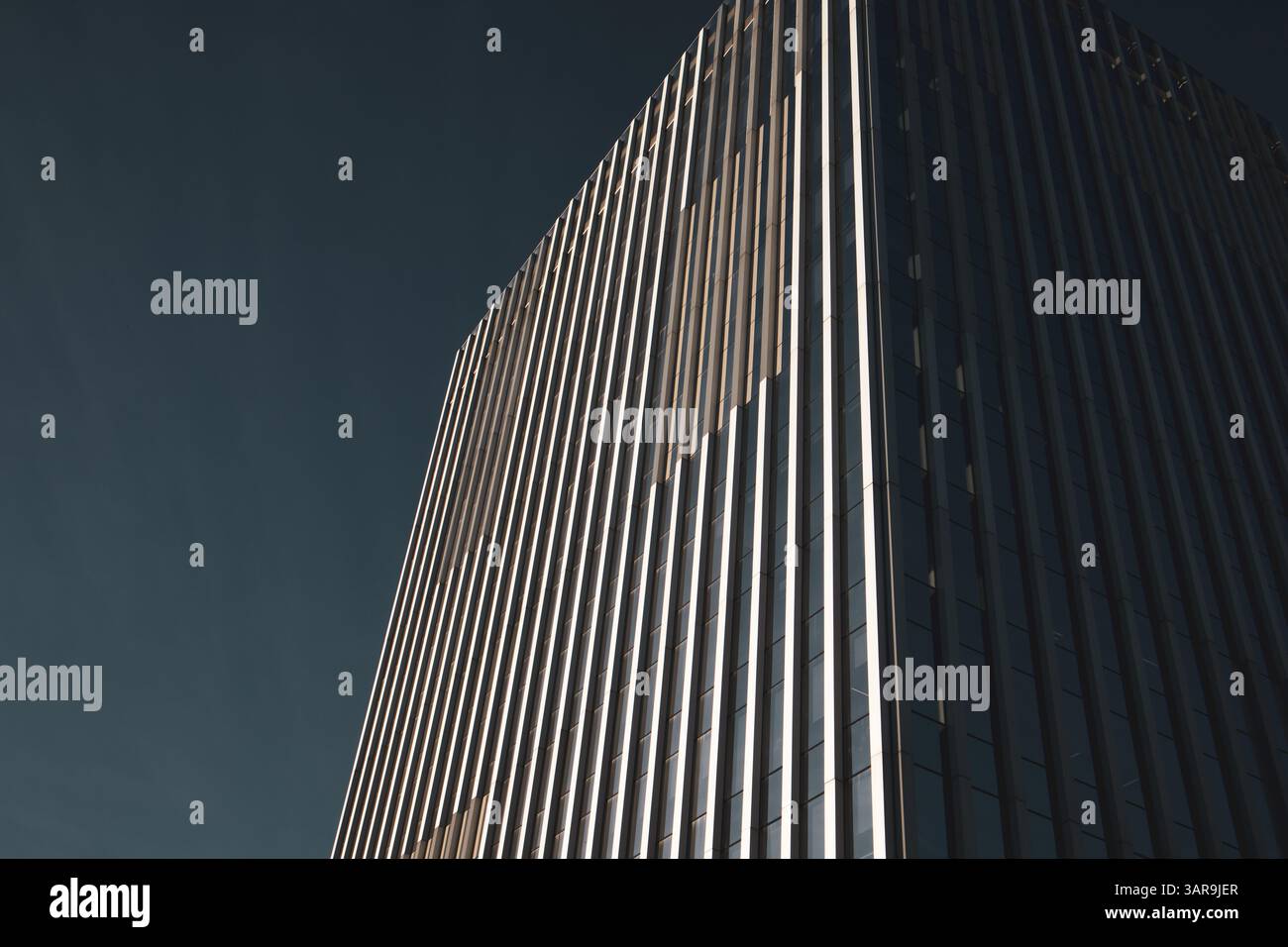 An impressive modern skyscraper reaches into a clear blue sky, showcasing architectural prowess and design. The building has sleek lines. Urban scene. Stock Photo