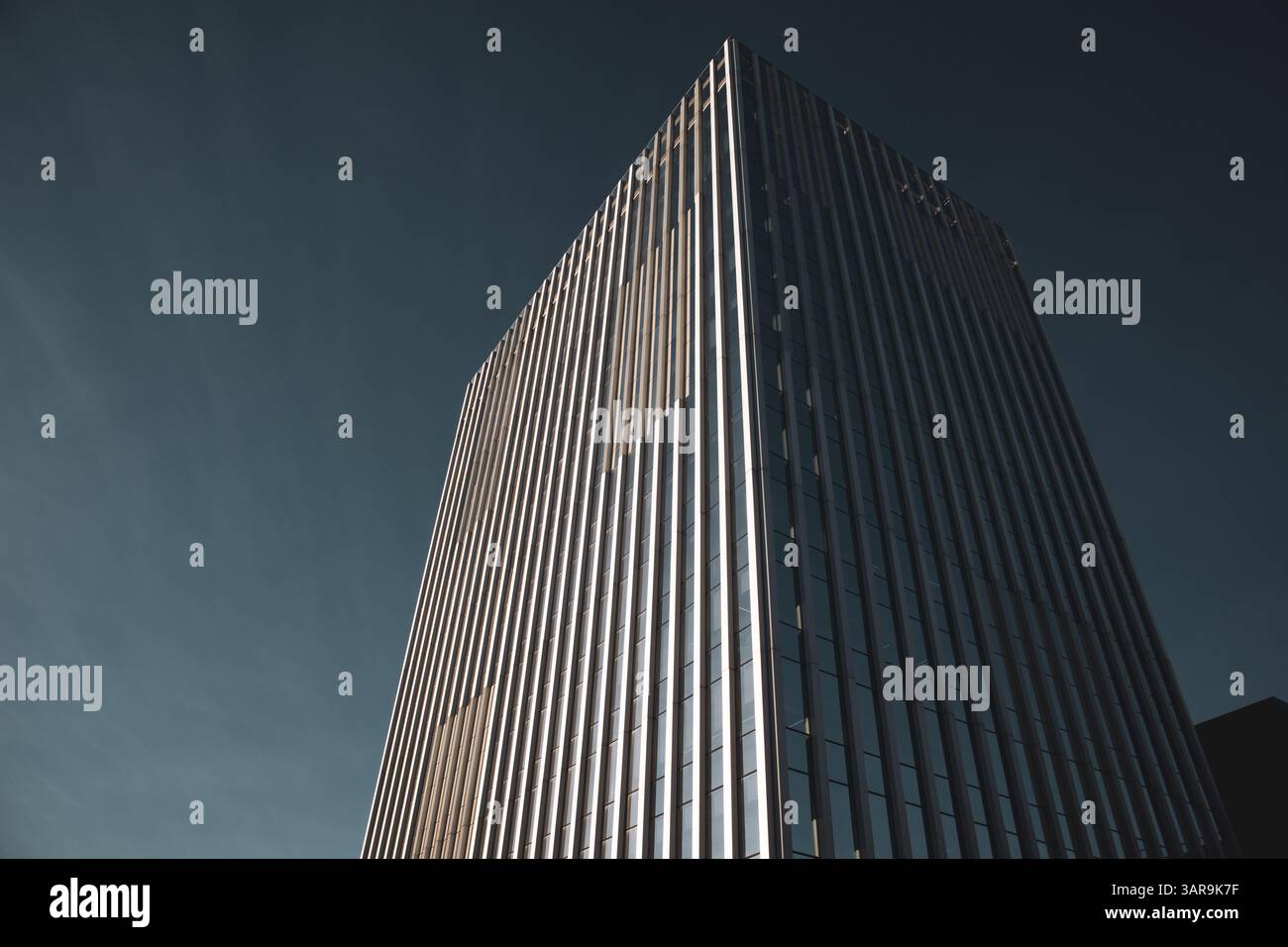 An impressive modern skyscraper reaches into a clear blue sky, showcasing architectural prowess and design. The building has sleek lines. Urban scene. Stock Photo