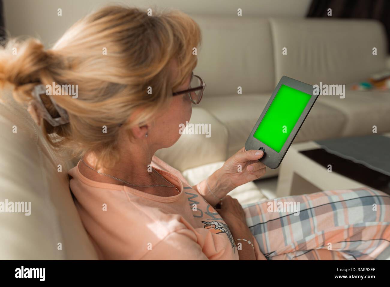 Senior woman using e-reader with green screen on couch Stock Photo