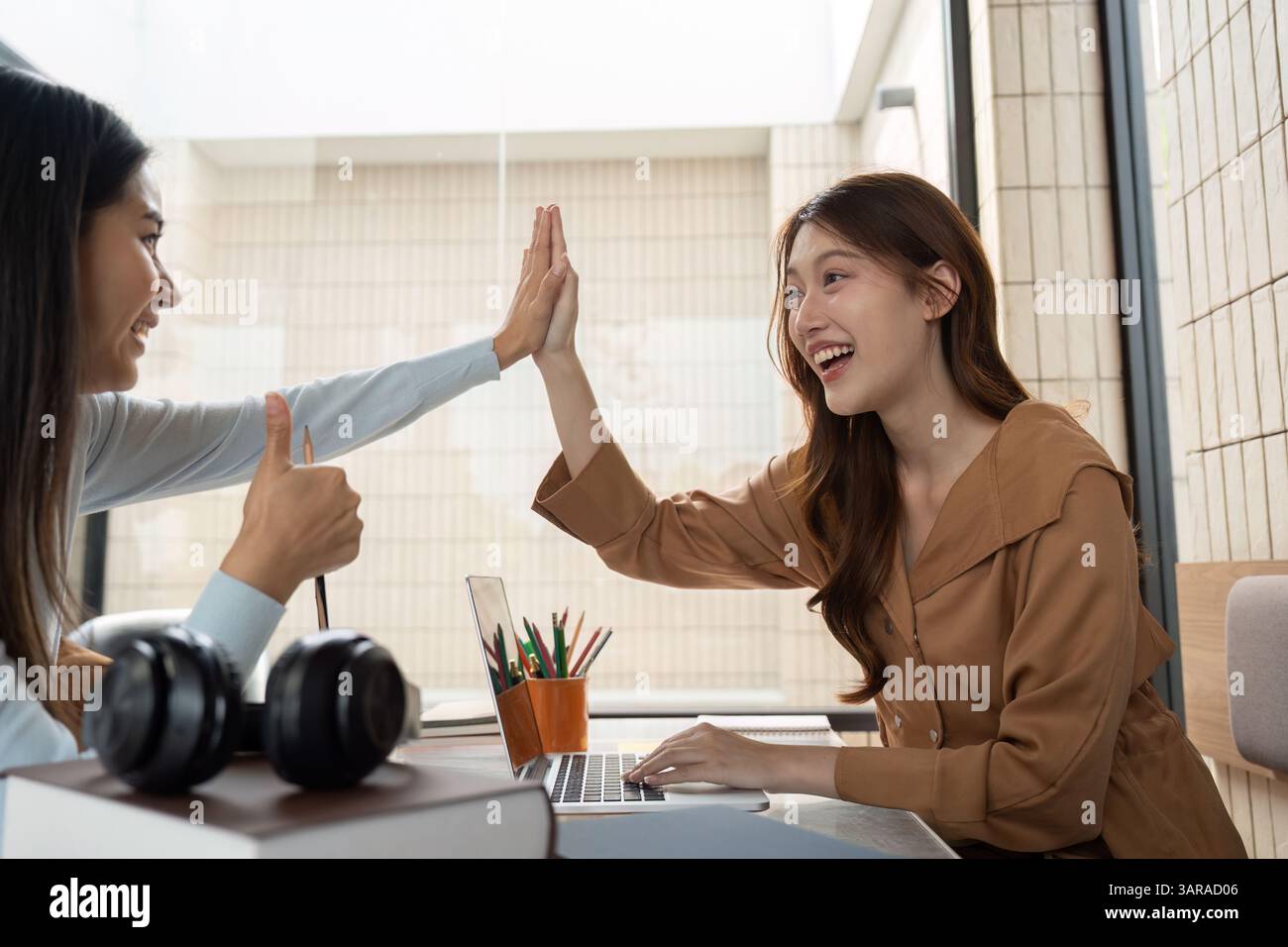 Joyful Learning and Collaboration. Two students share a high five, celebrating a successful study moment. Stock Photo