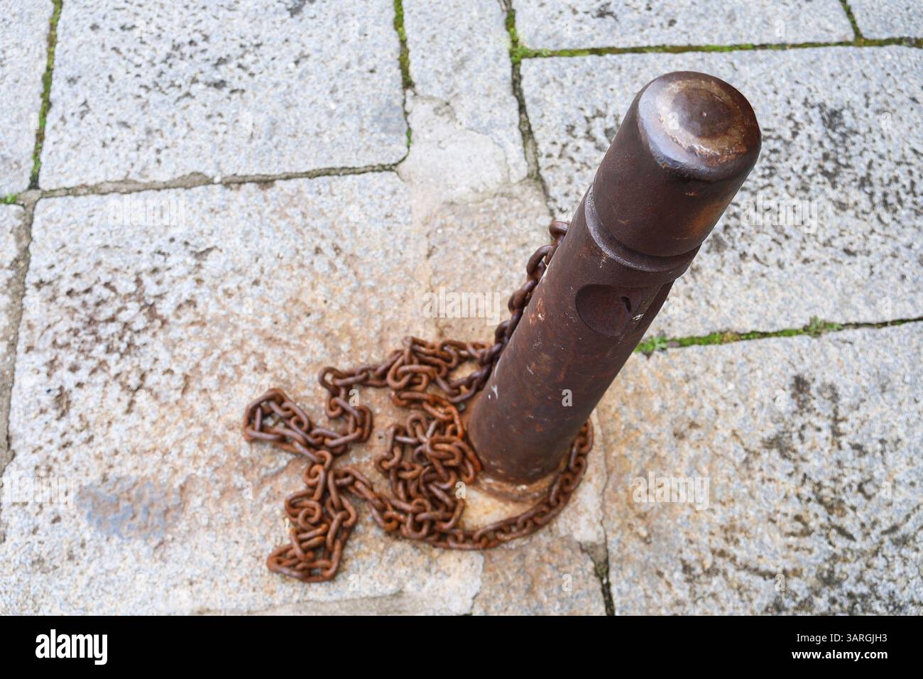 Security pivot with Rusty chains on stone floor on the street in Spain Stock Photo