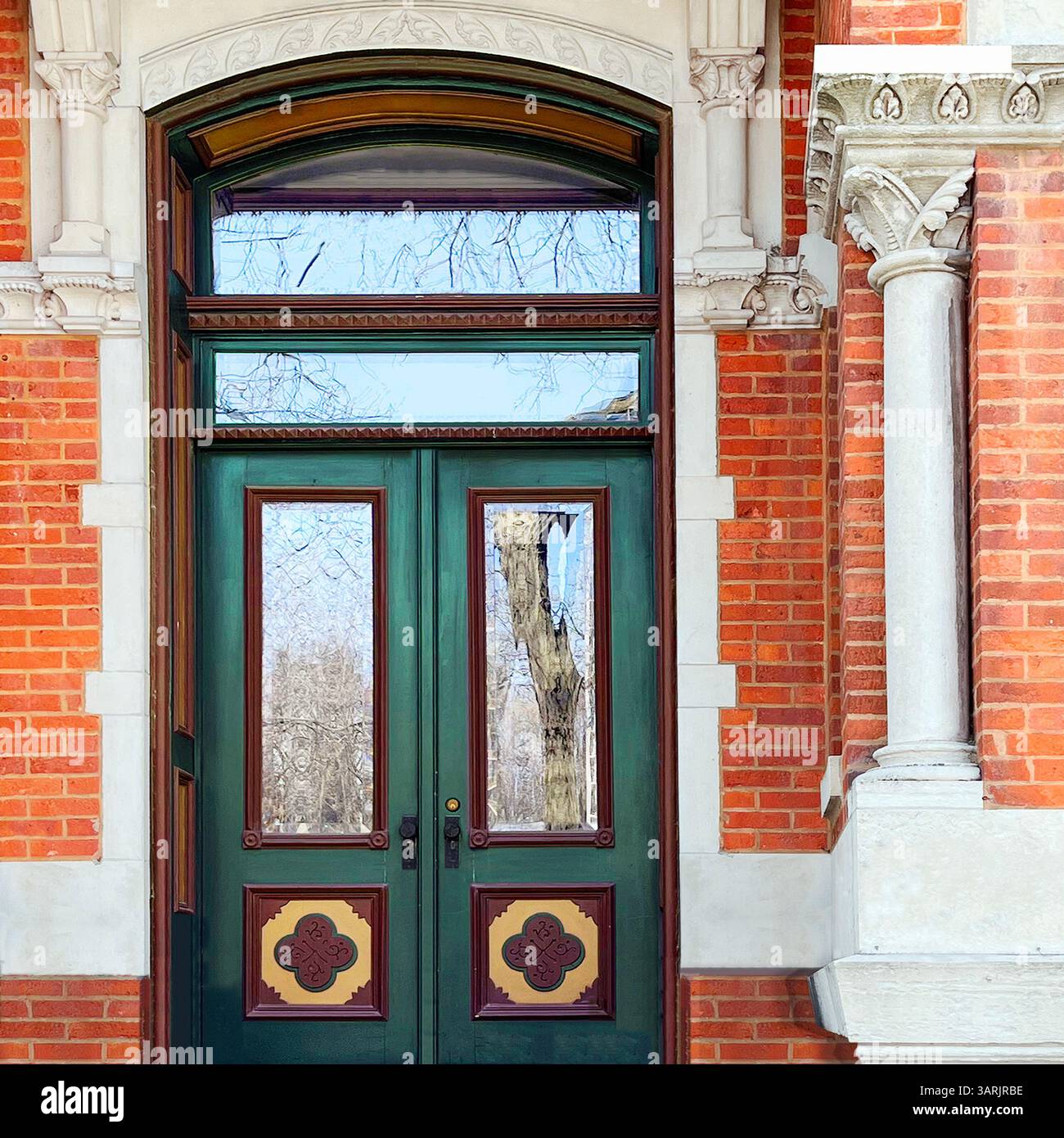 Decorative green double door with glass panels and ornate crest accents, framed by arched stonework and red brick in a historic Chicago building - Smartphone Captured Stock Image