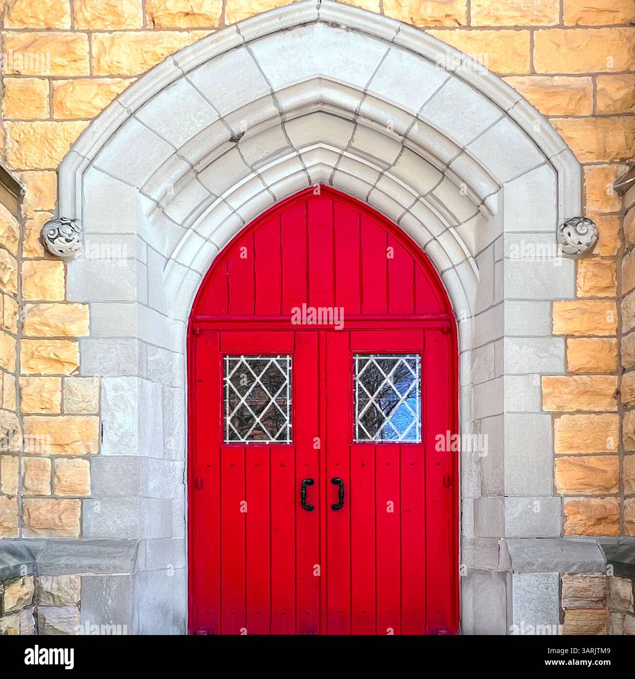 Red Gothic-style church door with diamond-pane windows, framed by a pointed stone arch and yellow limestone facade in Chicago. - Smartphone Captured Stock Image