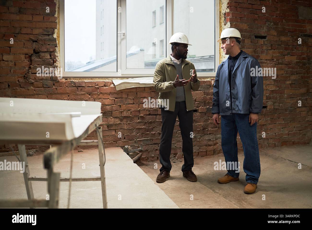 Two biracial builders having conversation while working at construction site together Stock Photo