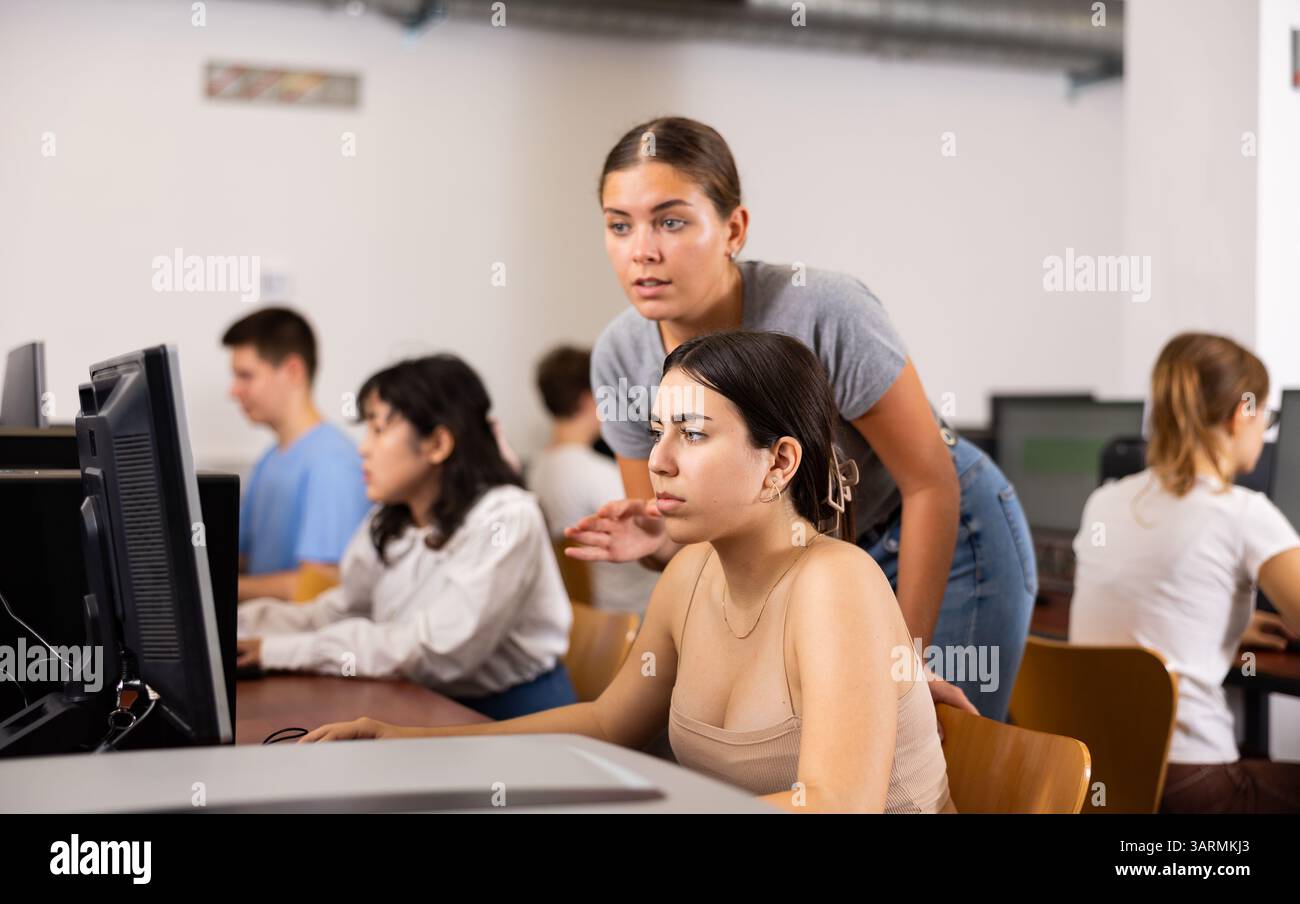 Schoolgirl using computer and teacher helping to him in class room ...