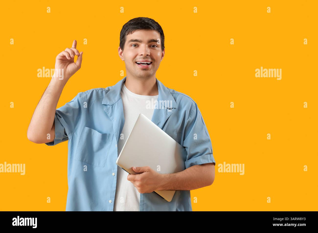 Male programmer with laptop pointing at something on orange background Stock Photo