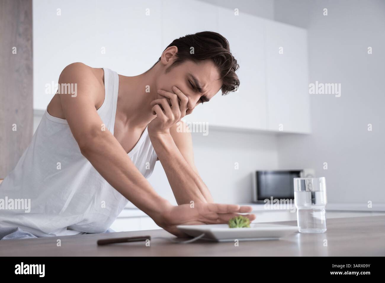 Young man with anorexia refusing from food in kitchen Stock Photo