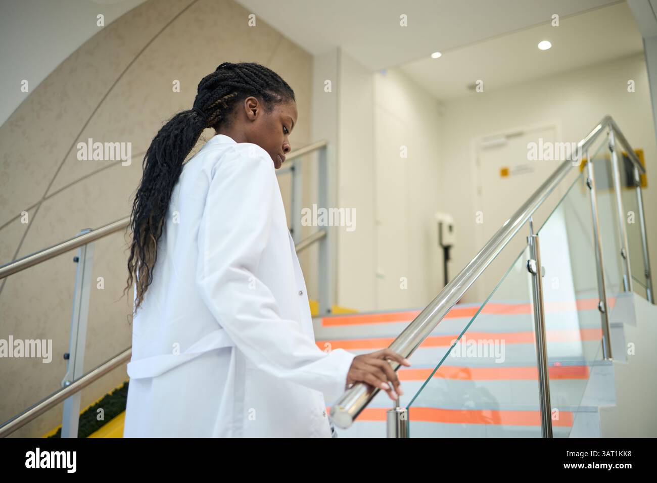 Professional wearing lab coat ascending stairs while holding railing in ...