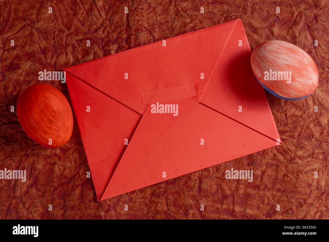 A vibrant red envelope sits on a hard surface with two colorful hand painted eggs. Stock Photo