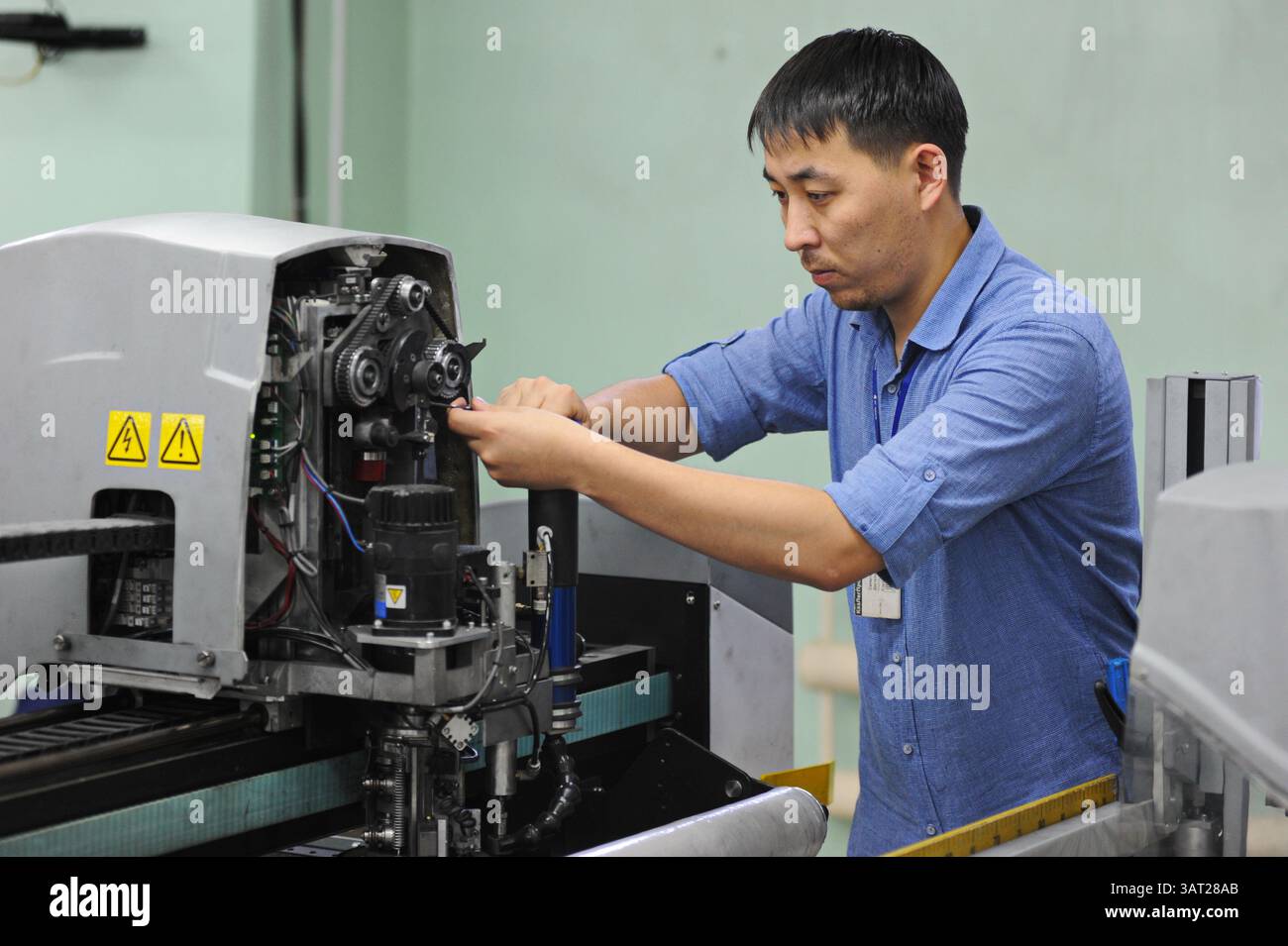 A worker repairs an embroidery machine in a sewing workshop Stock Photo