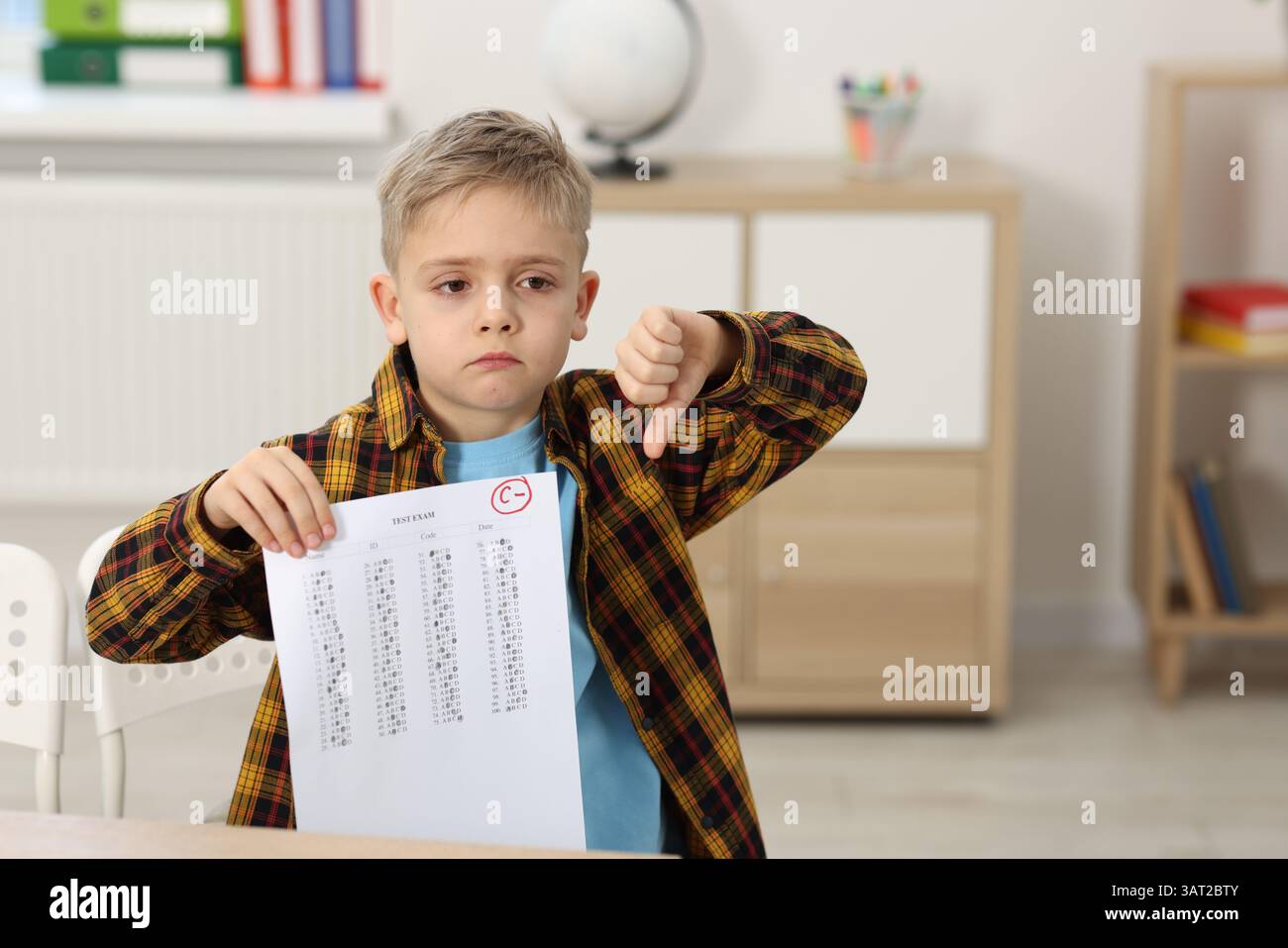 School grade. Sad boy holding answer sheet with letter C and minus symbol indoors, space for text Stock Photo