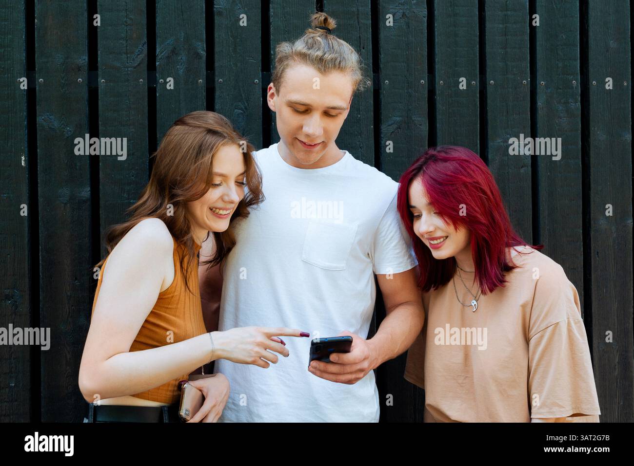 Three friends smiling while looking at a smartphone outside Stock Photo