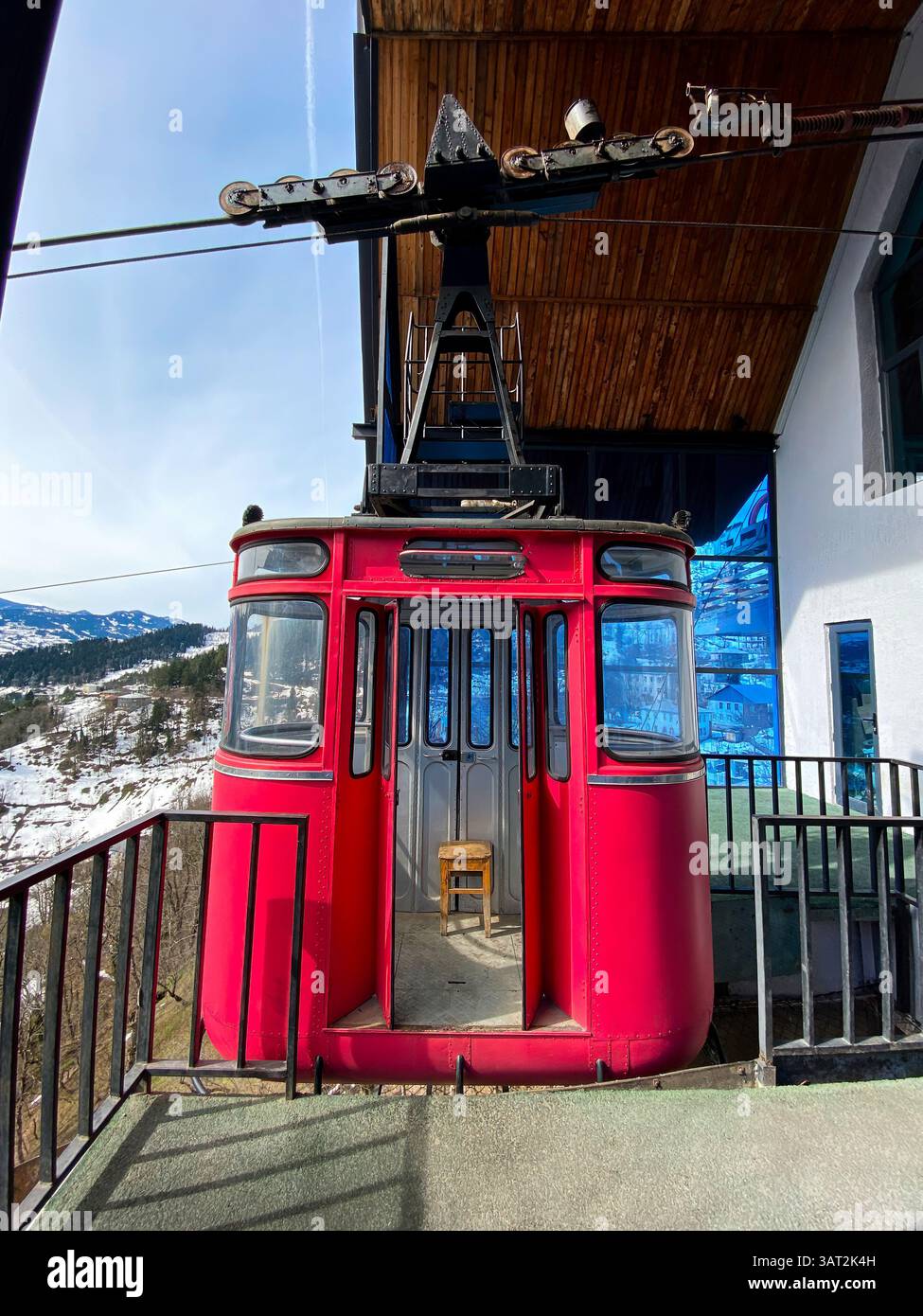 A red cable car parked at a mountain station with a snowy landscape and wooden roof in the background. - Smartphone Captured Stock Image