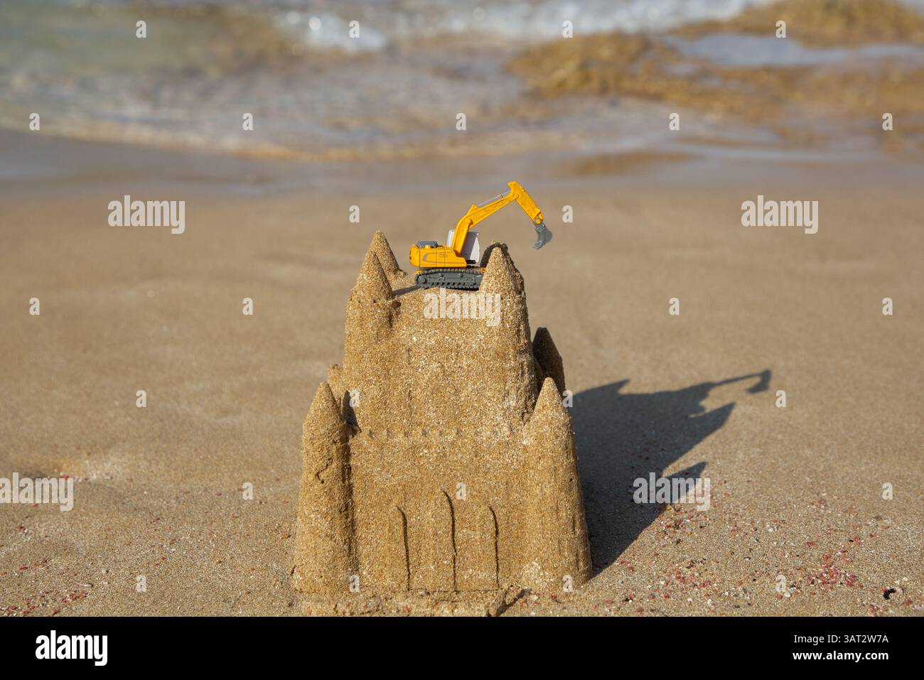 miniature orange toy excavator stands on a sand castle on the seashore ...