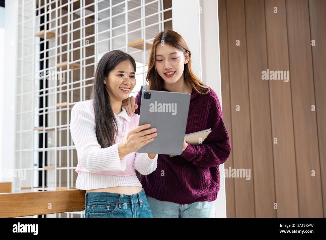 Study Time and Friendship. Two students sharing study materials while bonding over their digital device in a modern school setting. Stock Photo
