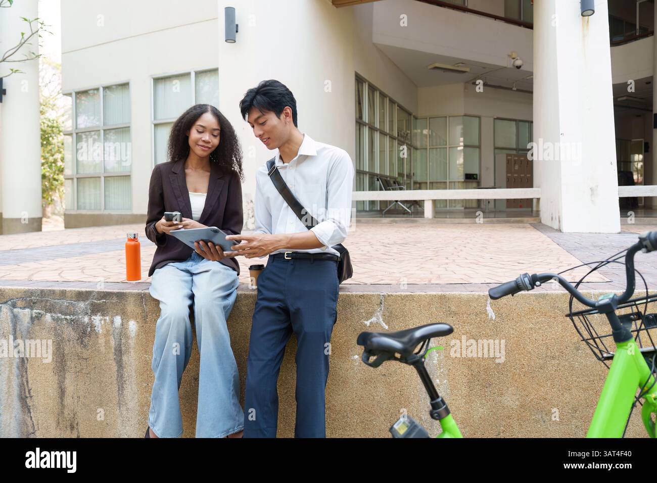 Sustainability and Collaboration. Two young professionals discussing eco-friendly initiatives over coffee and digital devices. Stock Photo