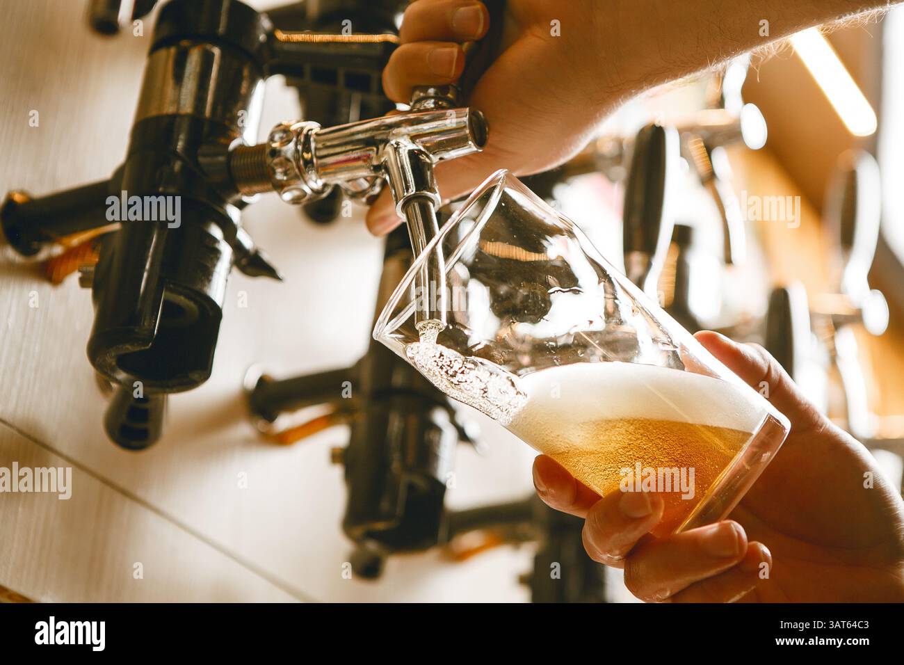 Pouring Golden Beer Into Glass From Tap in Well-Lit Bar at Afternoon Gathering Stock Photo