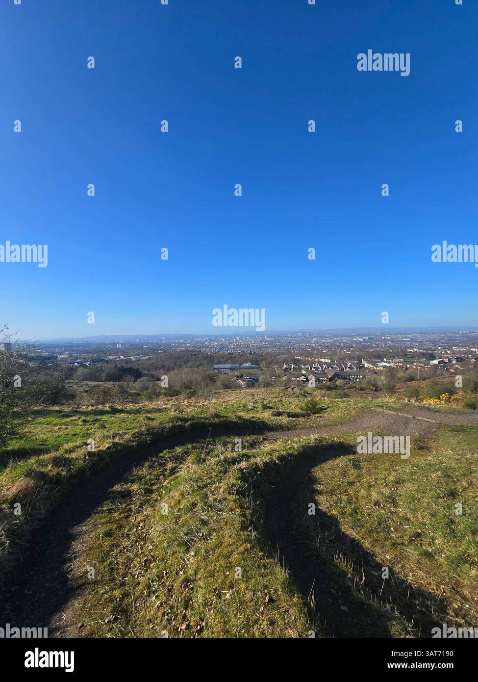 Sweeping view from Cathkin Braes, Glasgow, under a dazzling blue sky. Grassy slopes in the foreground offer a natural frame to the distant cityscape. - Smartphone Captured Stock Image