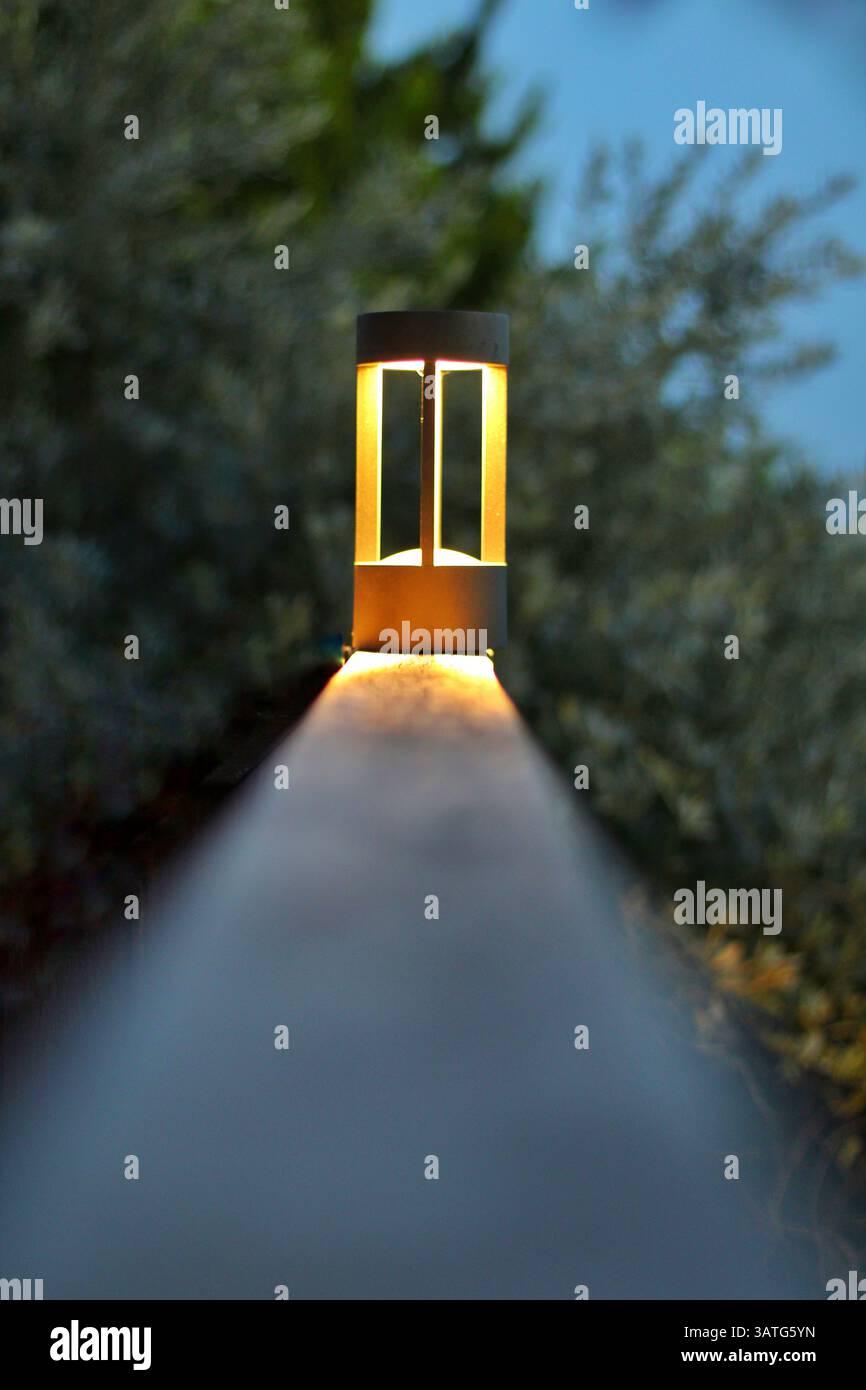 Modern outdoor lamp on a wooden railing, captured from a centered perspective at dusk. Ideal for themes of lighting, and peaceful evening ambiance. Stock Photo