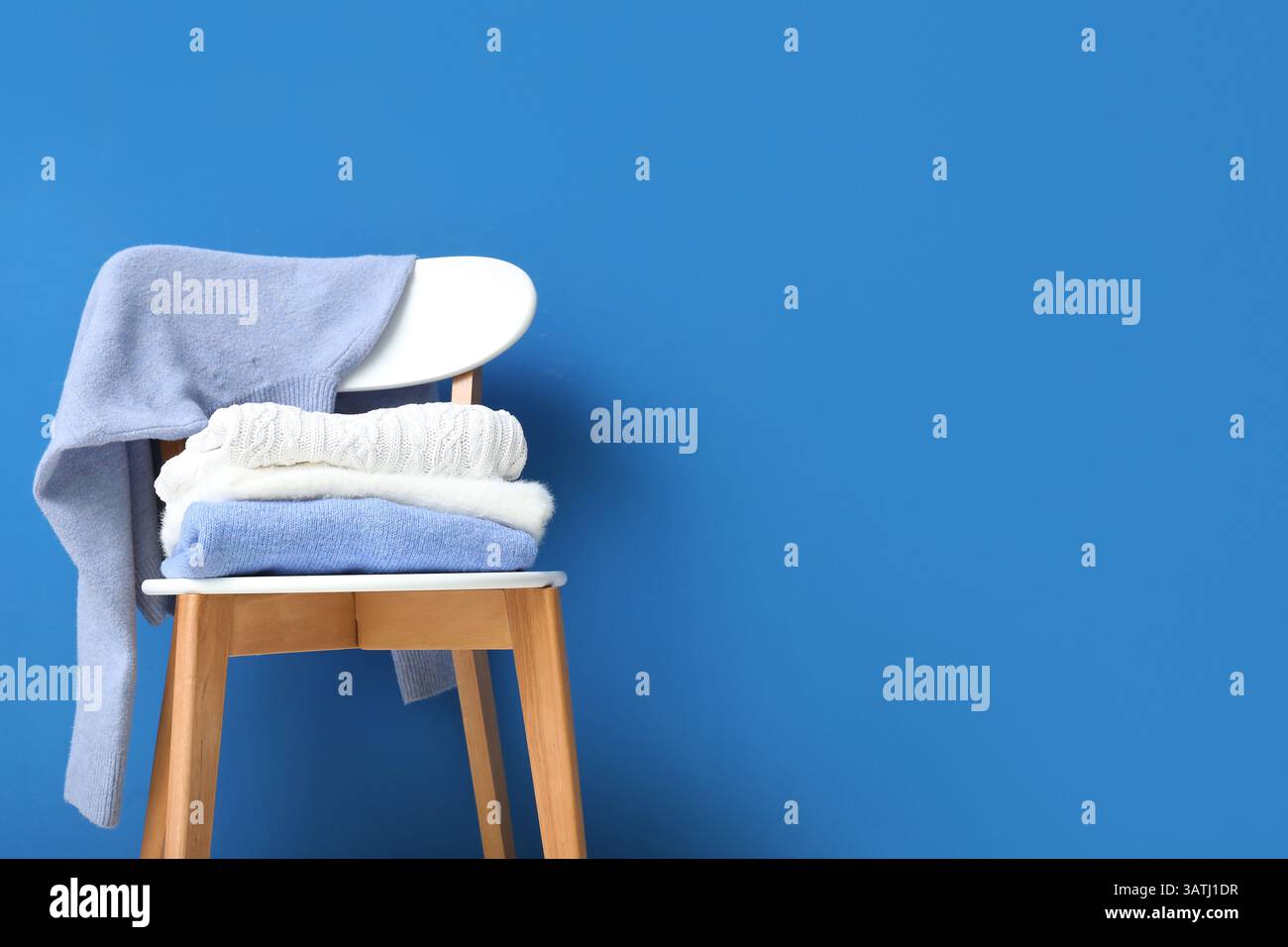 Stack of folded sweaters on chair against blue background Stock Photo