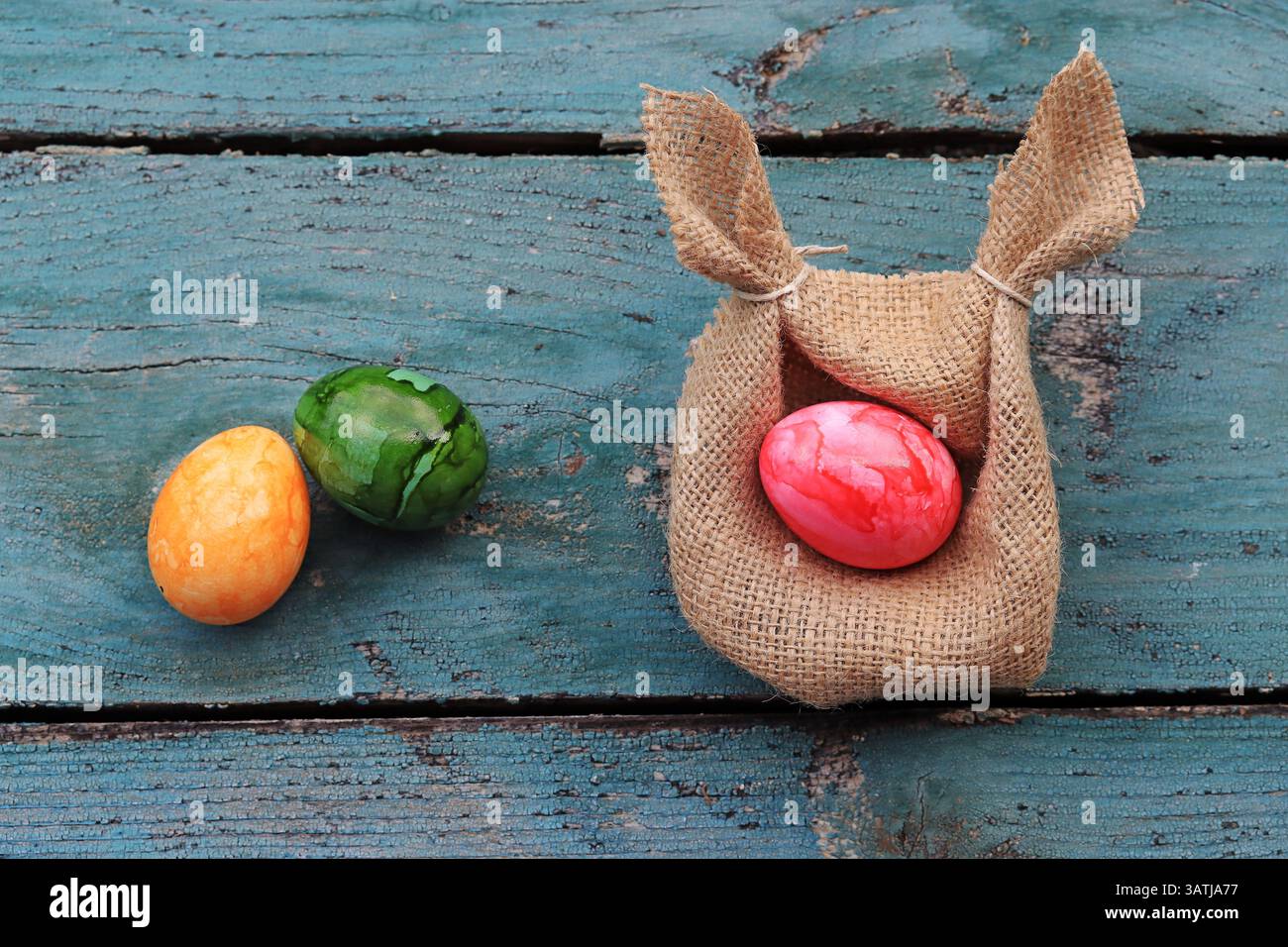 An Easter nest made from a jute sack with ears and colorful Easter eggs on a wooden base Stock Photo