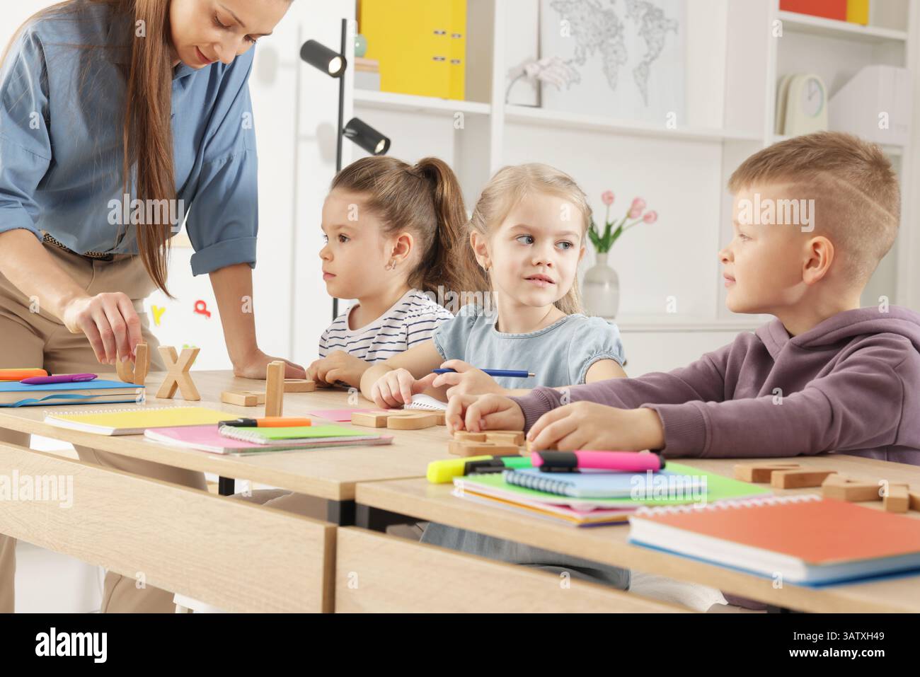 Children having lesson with teacher at desk indoors Stock Photo - Alamy