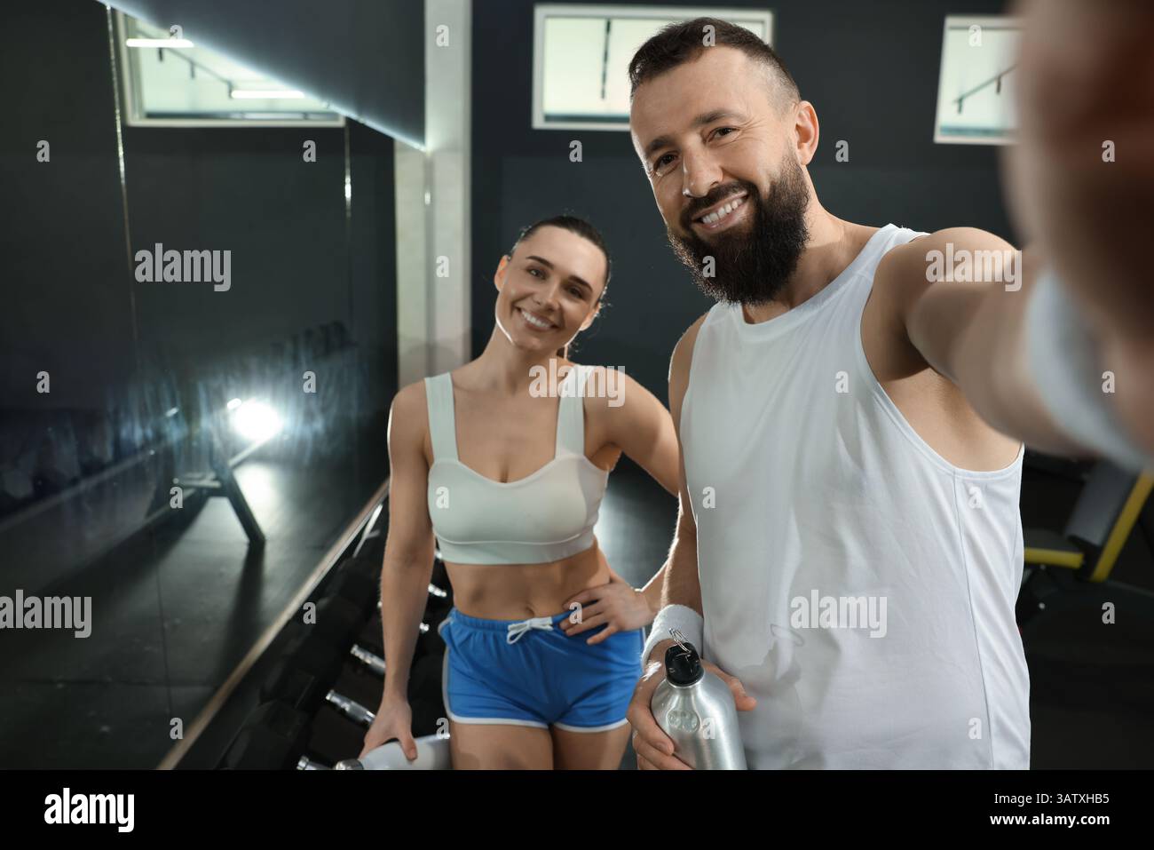 Couple with water bottles taking selfie after training in gym Stock Photo