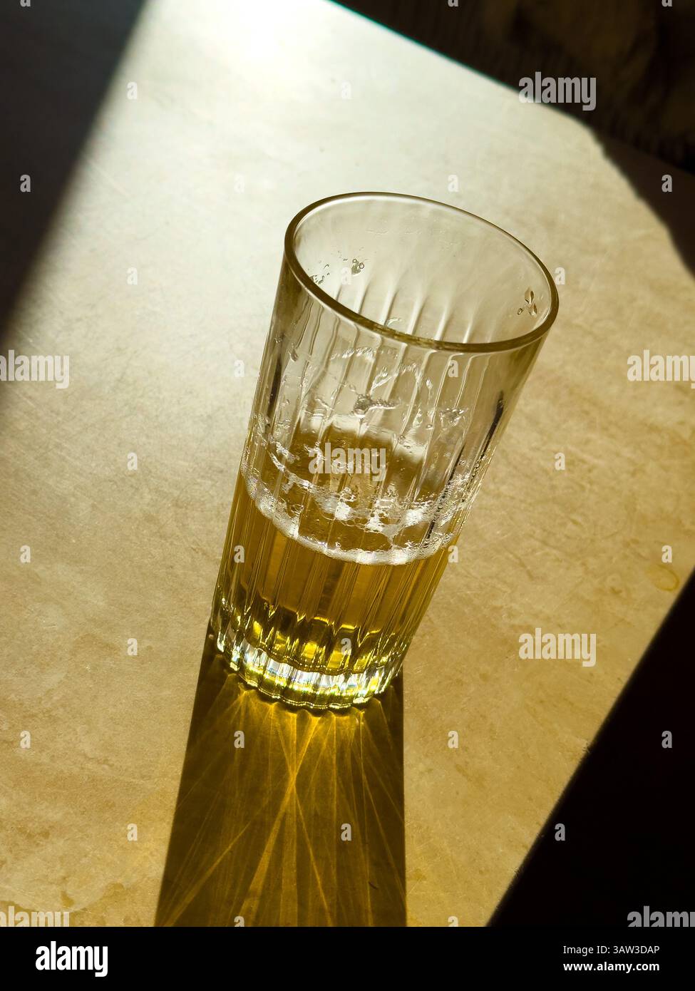 a halfdrunk glass of beer on a sunlit table - Smartphone Captured Stock Image