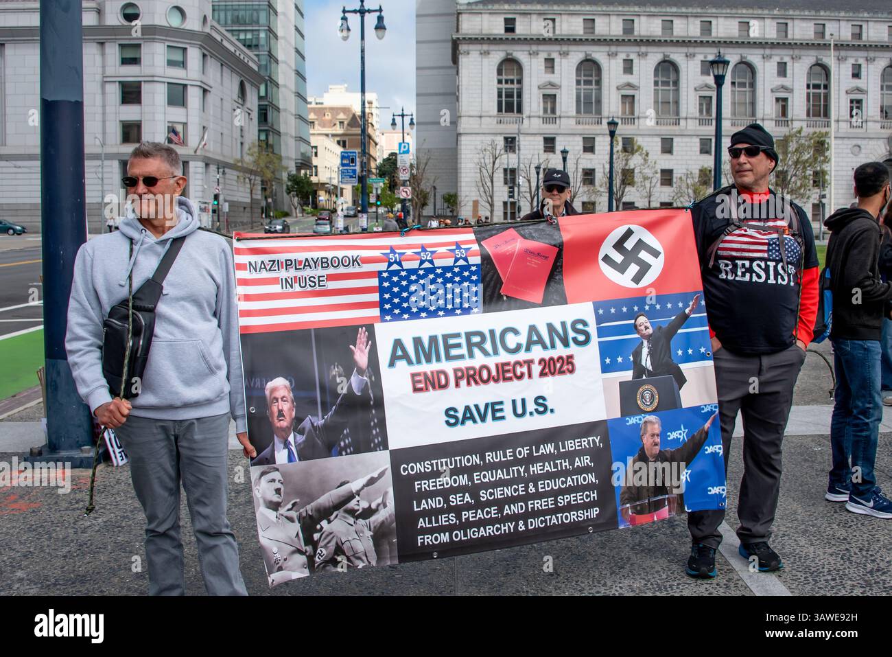 San Francisco, USA. 19th Apr 2025. Protesters gather at the Civic Center Plaza “Stop the Billionaire Agenda” protest against the Trump Administration. . Two men hold a large banner with an upside down American flag, Nazi flag, and photos of Donald Trump, Elon Musk, and Steve Bannon appearing with mustaches and Nazi salutes next to a photo of Hitler himself. The banner reads, 'Nazi Playbook in Use. Americans End Project 2025. Save U.S.' Credit: Shelly Rivoli/Alamy Live News - Stock Image