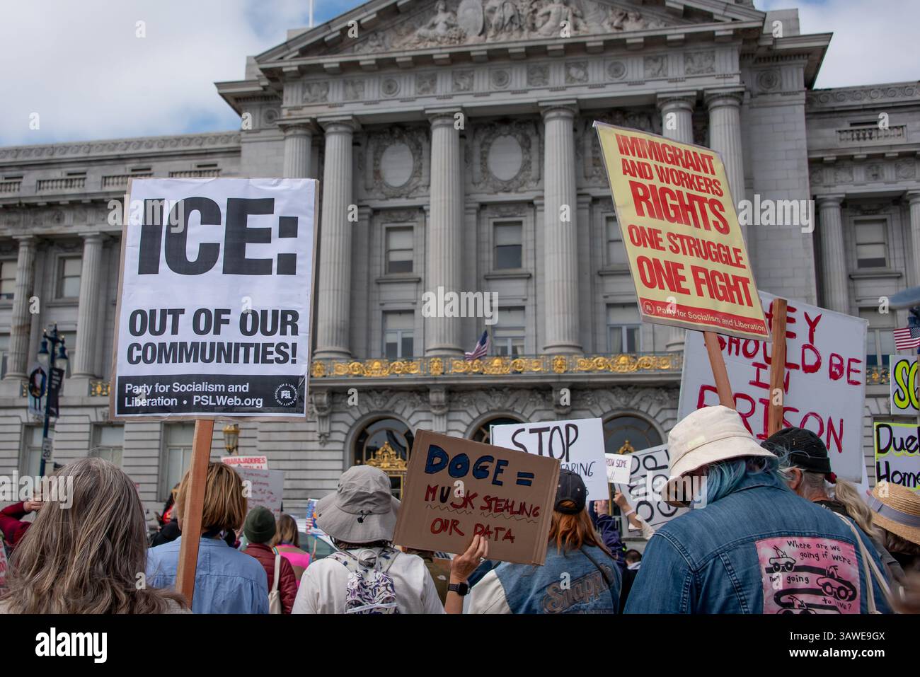 San Francisco, USA. 19th Apr 2025. Protesters stand before San Francisco City Hall at the Civic Center Plaza “Stop the Billionaire Agenda” protest against the Trump Administration. Signs held above their heads read, 'ICE: Out of our communities!' 'DOGE = Musk stealing our data,' and 'Immigrant and workers rights, One struggle, One fight.' Credit: Shelly Rivoli/Alamy Live News - Stock Image