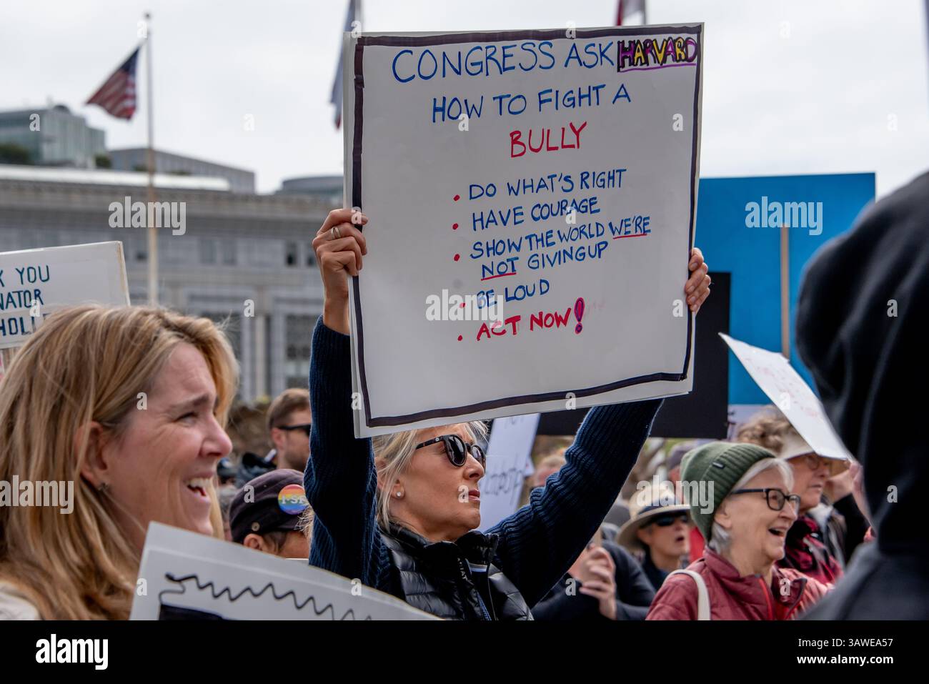 San Francisco, USA. 19th Apr 2025. Protesters crowd Civic Center Plaza for the “Stop the Billionaire Agenda” protest against the Trump Administration. A woman holds a sign high reading, 'Congress ask Harvard how to fight a bully. Do what's right, have courage, show the world we're not giving up, be loud, act now!' Credit: Shelly Rivoli/Alamy Live News - Stock Image