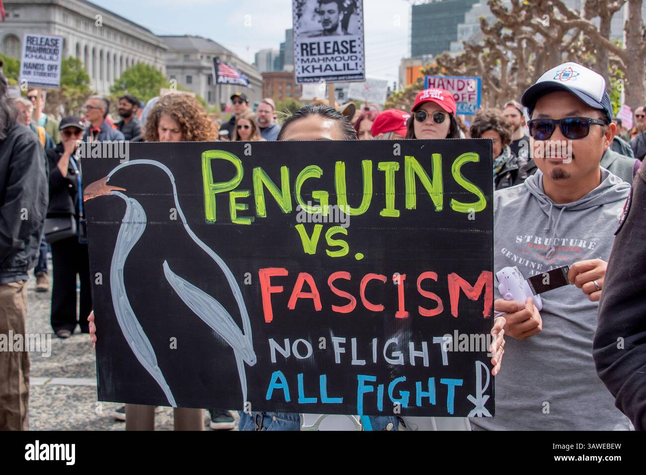 San Francisco, USA. 19th Apr 2025. Among the crowd, a protester holds a sign reading, 'Penguins vs. fascism.  No flight. All fight,' at the Civic Center Plaza “Stop the Billionaire Agenda” protest against the Trump Administration. More signs are seen in the background including, 'Release Mahmoud Khalil!' Credit: Shelly Rivoli/Alamy Live News - Stock Image