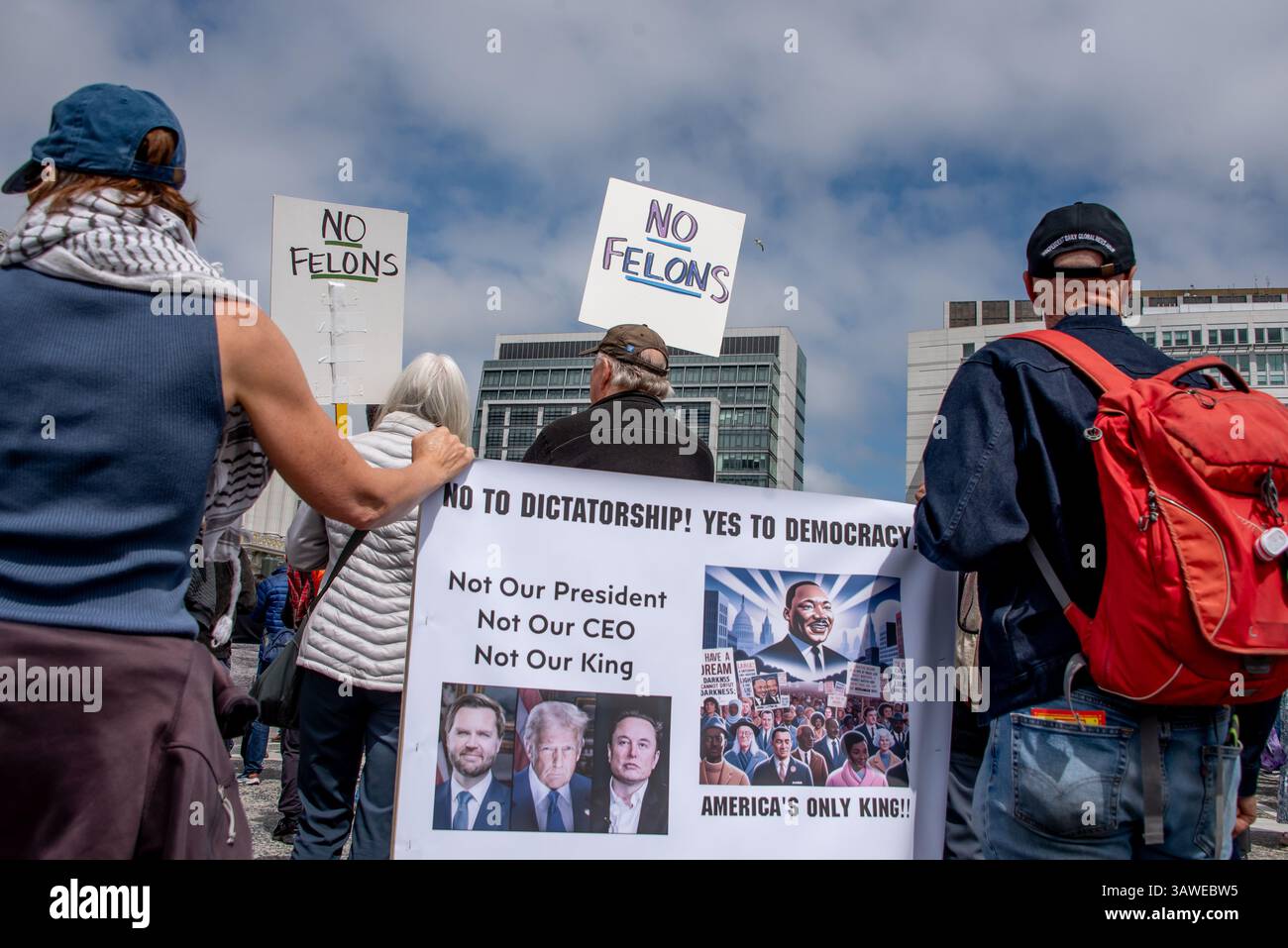 San Francisco, USA. 19th Apr 2025. Protesters gather to listen to spearkers at the Civic Center Plaza “Stop the Billionaire Agenda” protest against the Trump Administration. Two signs reading, 'No felons,' are held above a wide sign reading, 'No to Dictatorship! Yes to Democracy.,' and beside photos of Vance, Trump, and Musk, an illustration of Martin Luther King Jr. appears above the words, 'America's only king!'  Credit: Shelly Rivoli/Alamy Live News - Stock Image