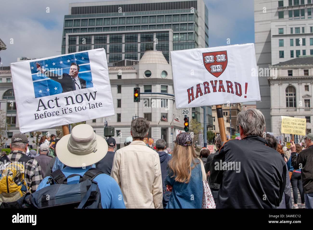 San Francisco, USA. 19th Apr 2025. Protesters crowd Civic Center Plaza for the “Stop the Billionaire Agenda” protest against the Trump Administration.One sign held hgih reads, 'Act now, before it's too late,' with a picture of Elon Musk making a Nazi salute, while another sign reads, 'Harvard!' Credit: Shelly Rivoli/Alamy Live News - Stock Image