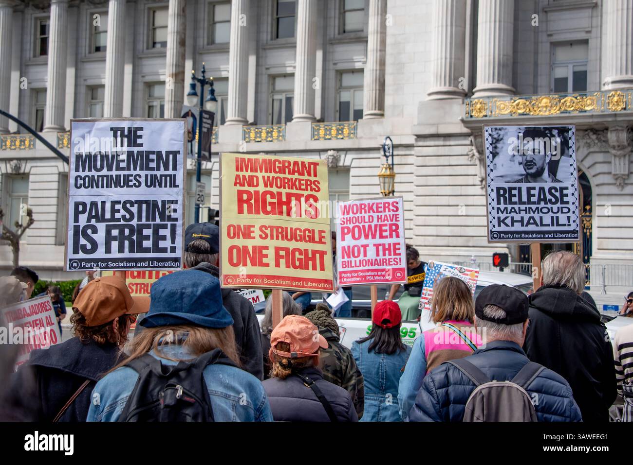 San Francisco, USA. 19th Apr 2025. Protesters listen to speakers in front of San Francisco City hall during the “Stop the Billionaire Agenda” protest against the Trump Administration.   Above the protesters, protest signs read, 'The movement continues until Palestine is free!' 'Immigrant and workers rights, one struggle, one fight,' 'Workers should have power, not the billionaires!' and 'Release Mahmoud Khalil!' Credit: Shelly Rivoli/Alamy Live News - Stock Image